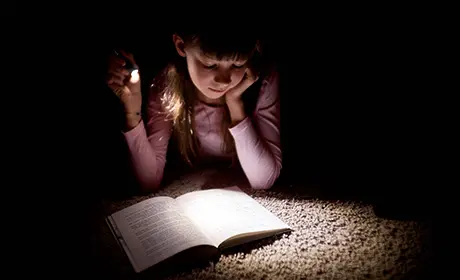 Fotografi som visar en ung flicka som läser bok i ljussken från en ficklampa.