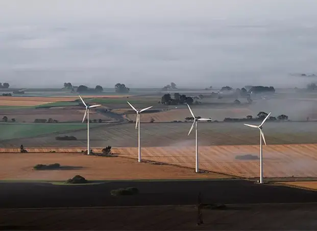 Fotografi som visar fyra vindkraftverk som står på fält i öppet landskap.